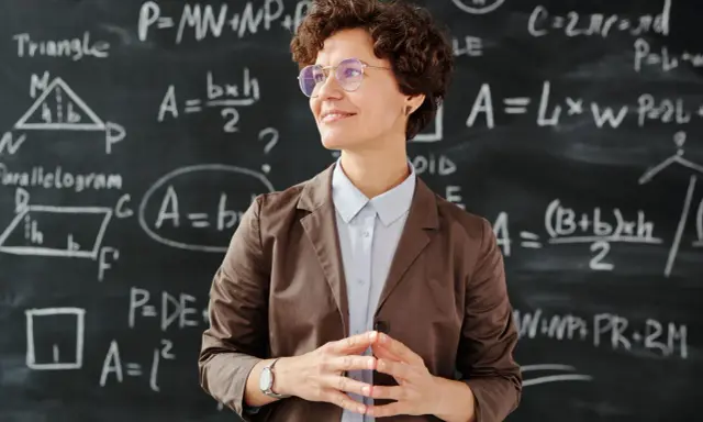Lehrerin vor Tafel mit Matheformeln. Sie fragt sich, wie viel verdienen Grundschullehrer.