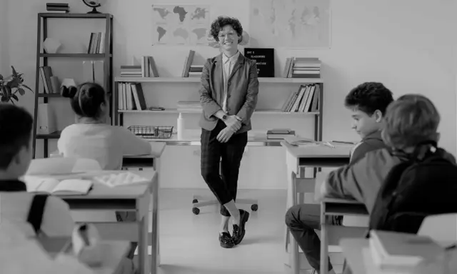 Lehrerin lächelt in einem Klassenzimmer, während Schüler an ihren Tischen sitzen. Eine Szene, die eine gute Klassengemeinschaft widerspiegelt.