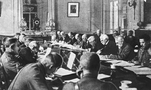 Männer in einem prunkvollen Raum diskutieren den Inhalt des Versailler Vertrags.