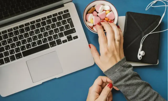 Eine Hand greift nach Süßigkeiten neben einem Laptop. Das Bild symbolisiert assoziatives Lernen: Belohnung und Fokus.