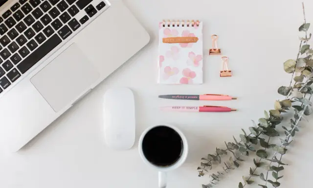 Ein Schreibtisch mit Laptop, Maus, Notizbuch, Stiften und Kaffee. Ideal für Lehrer, die ihr Zeitmanagement verbessern wollen.