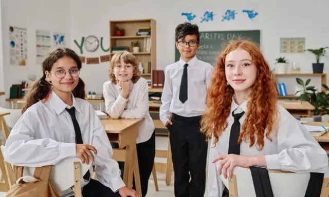Vier Schüler in weißem Hemd und schwarzer Krawatte im Klassenzimmer. Ein Vergleich des Schulsystems Finnland und Deutschland könnte hier beginnen.
