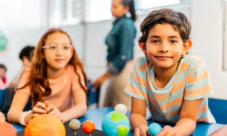 Kinder lernen spielerisch über das Sonnensystem. Ein Junge hält eine Himmelskugel, während ein Mädchen mit einem Modell des Sonnensystems experimentiert. Dies sind Beispiele für alternative Schulkonzepte.