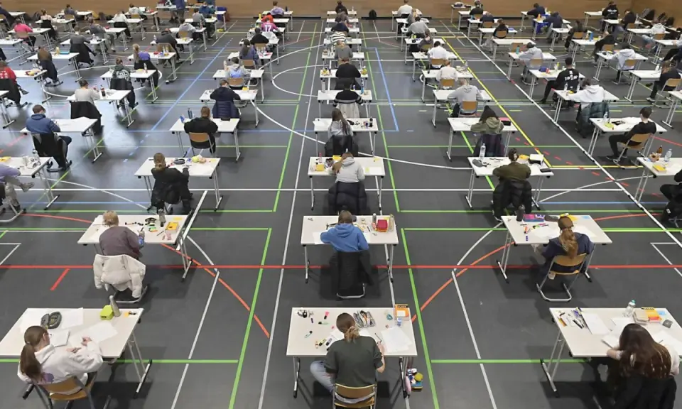 Viele Schüler sitzen in einer Sporthalle an Tischen, um zum Abitur zu schreiben.