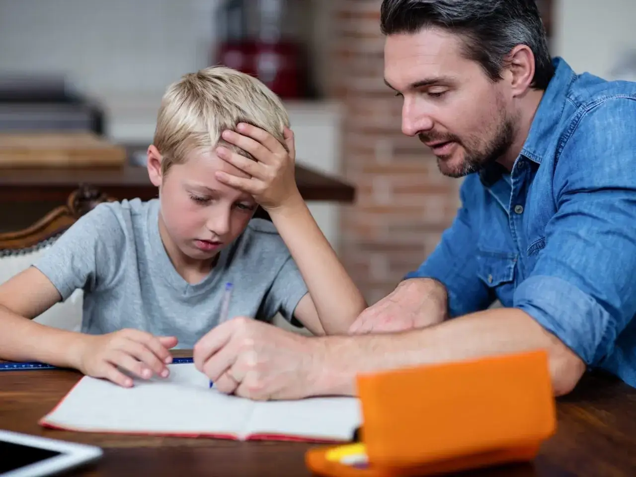 Ein Vater hilft seinem Sohn, der mit Lernschwierigkeiten kämpft, bei den Hausaufgaben. Der Junge wirkt frustriert, während der Vater ihn geduldig unterstützt.