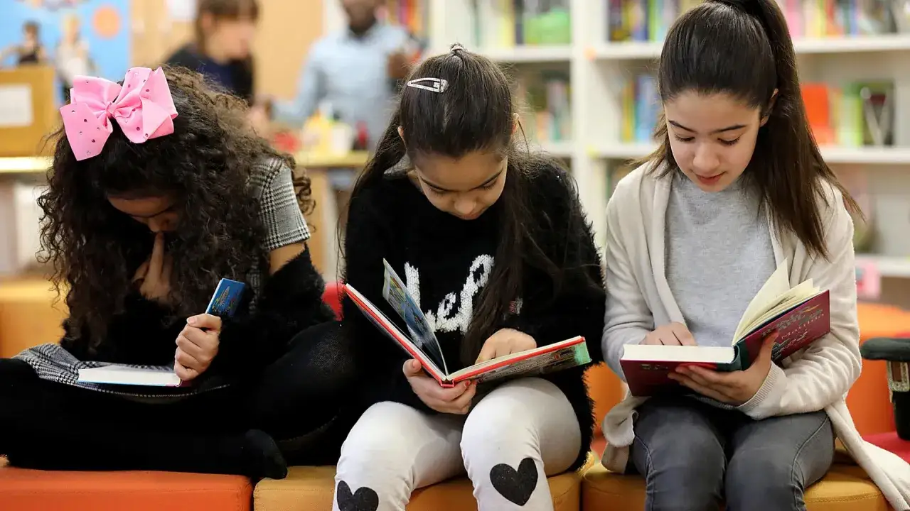 Drei Mädchen vertieft in Bücher. Ein Beispiel für Leseförderung in der Grundschule, das die Freude am Lesen zeigt.