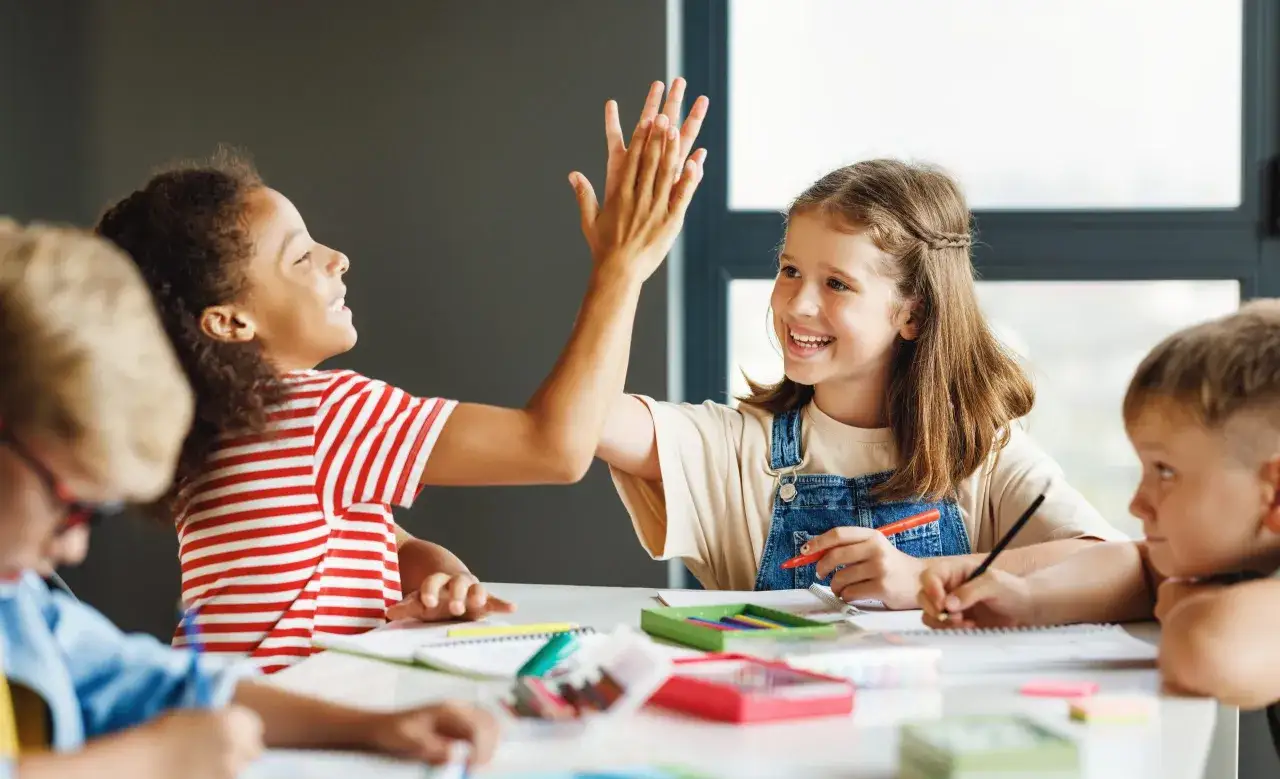 Kinder geben sich High-Five bei der Gruppenarbeit. Kreative Methoden fördern den Lernerfolg.