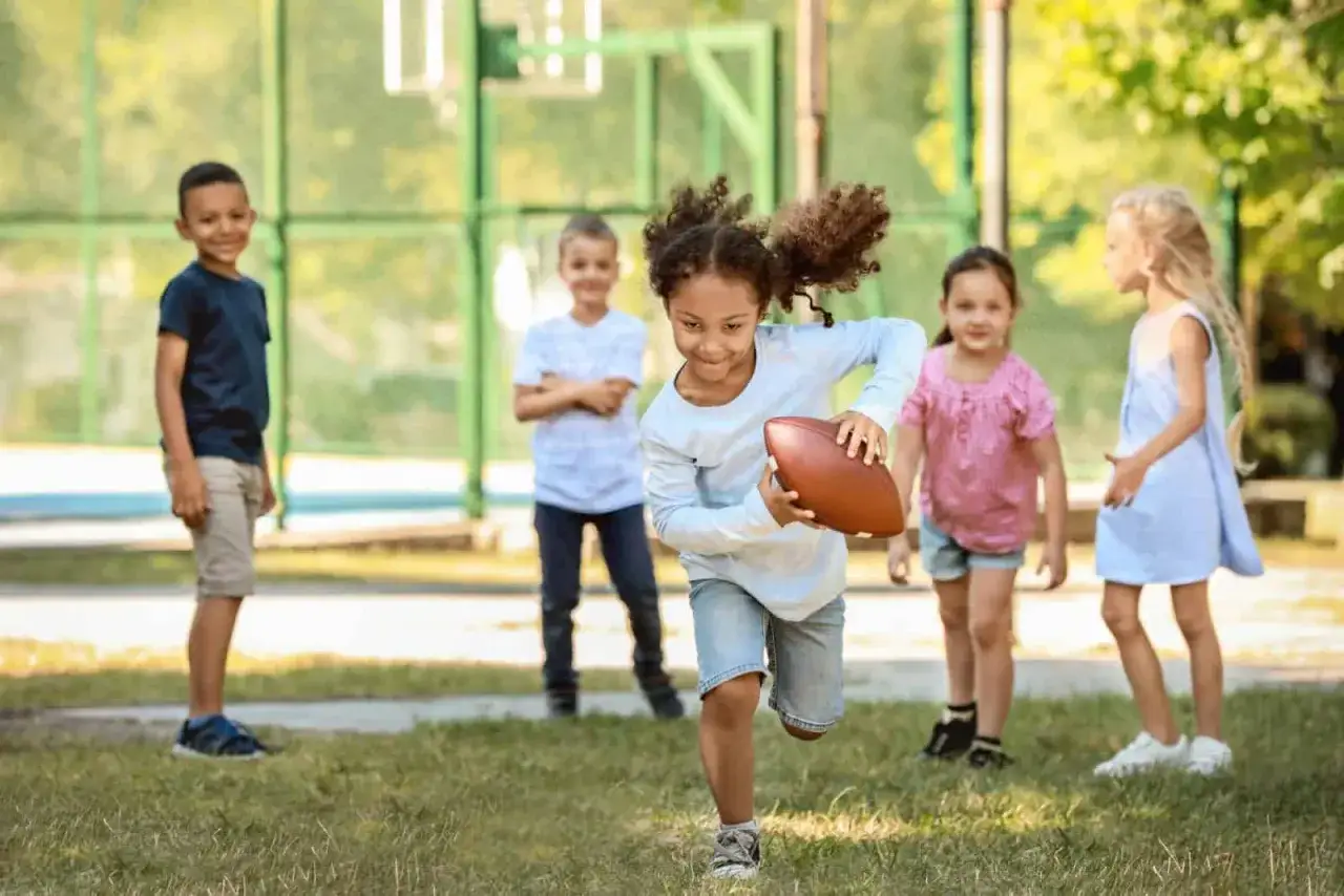 Kinder spielen auf dem Schulhof mit einem Football. Tolle Bewegungsspiele Grundschule für Spaß und Sport.