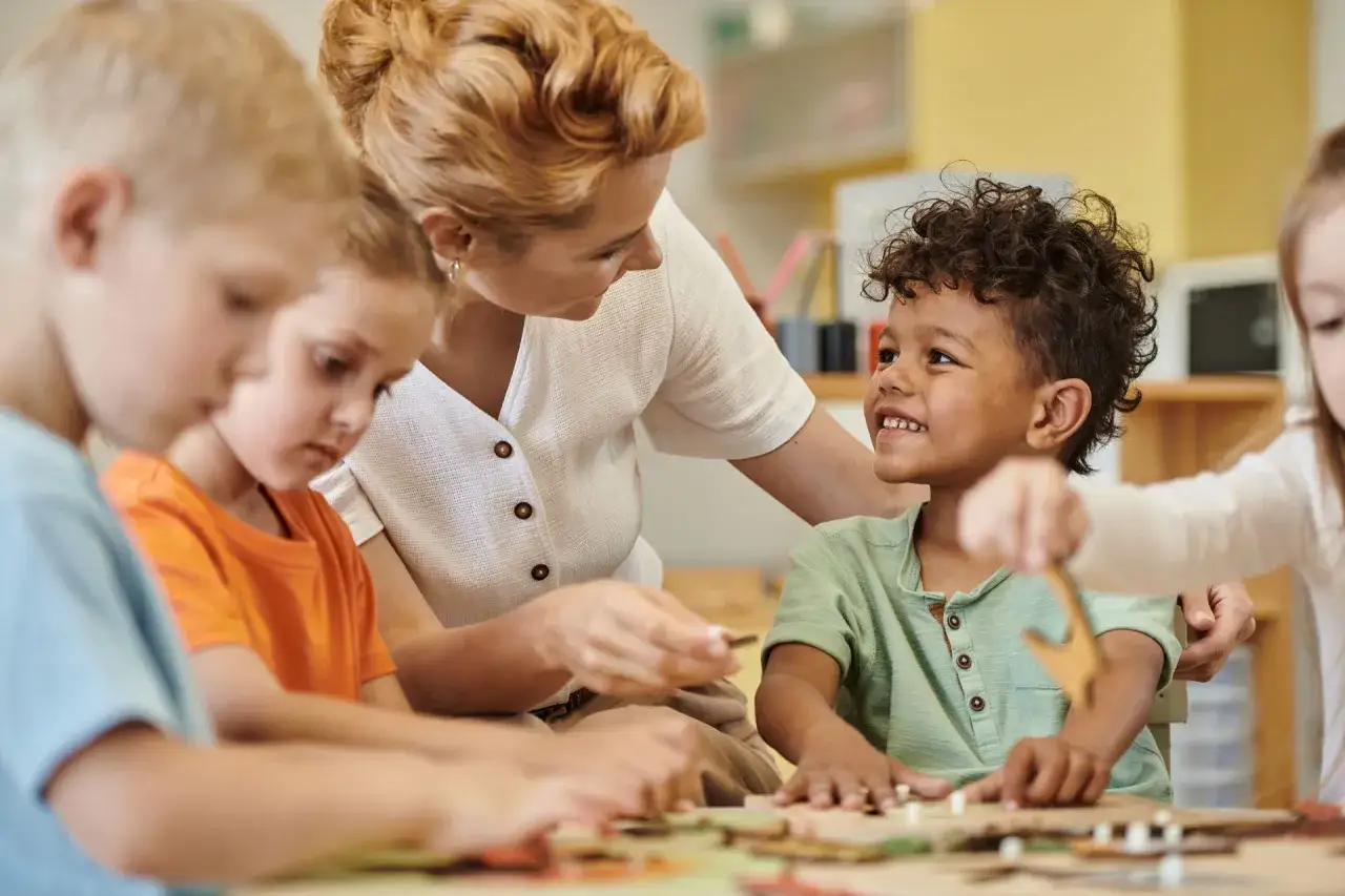 Lehrerin fördert vorurteilsbewusste Pädagogik, indem sie Kindern unterschiedlicher Herkunft beim Basteln hilft.