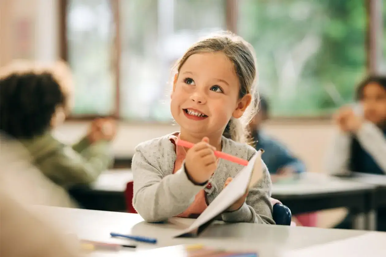 Ein Mädchen lernt mit einem Privatlehrer statt Schule in Deutschland. Sie lächelt und hält einen Stift.