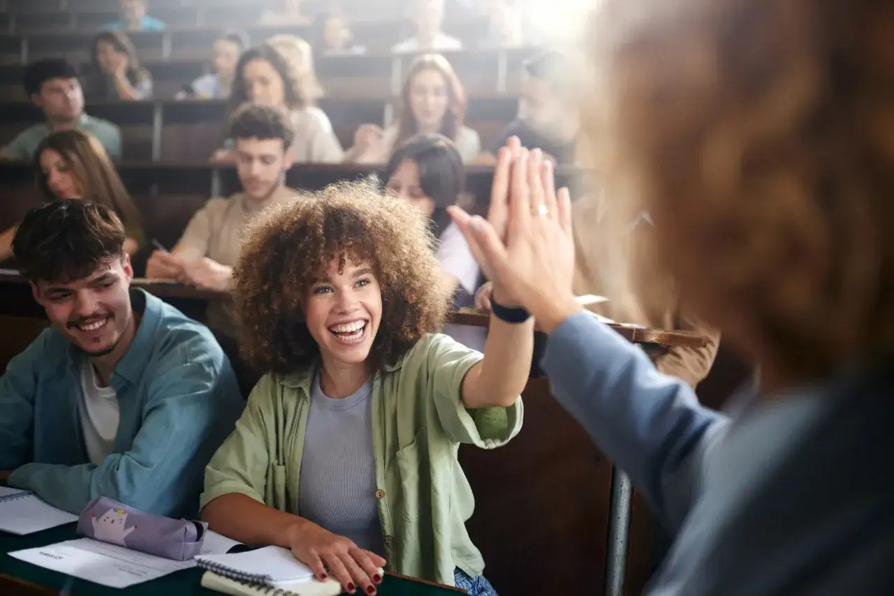 Studentin gibt High-Five im Hörsaal. Erfolgreiche Lernstrategien fördern Motivation und Engagement.