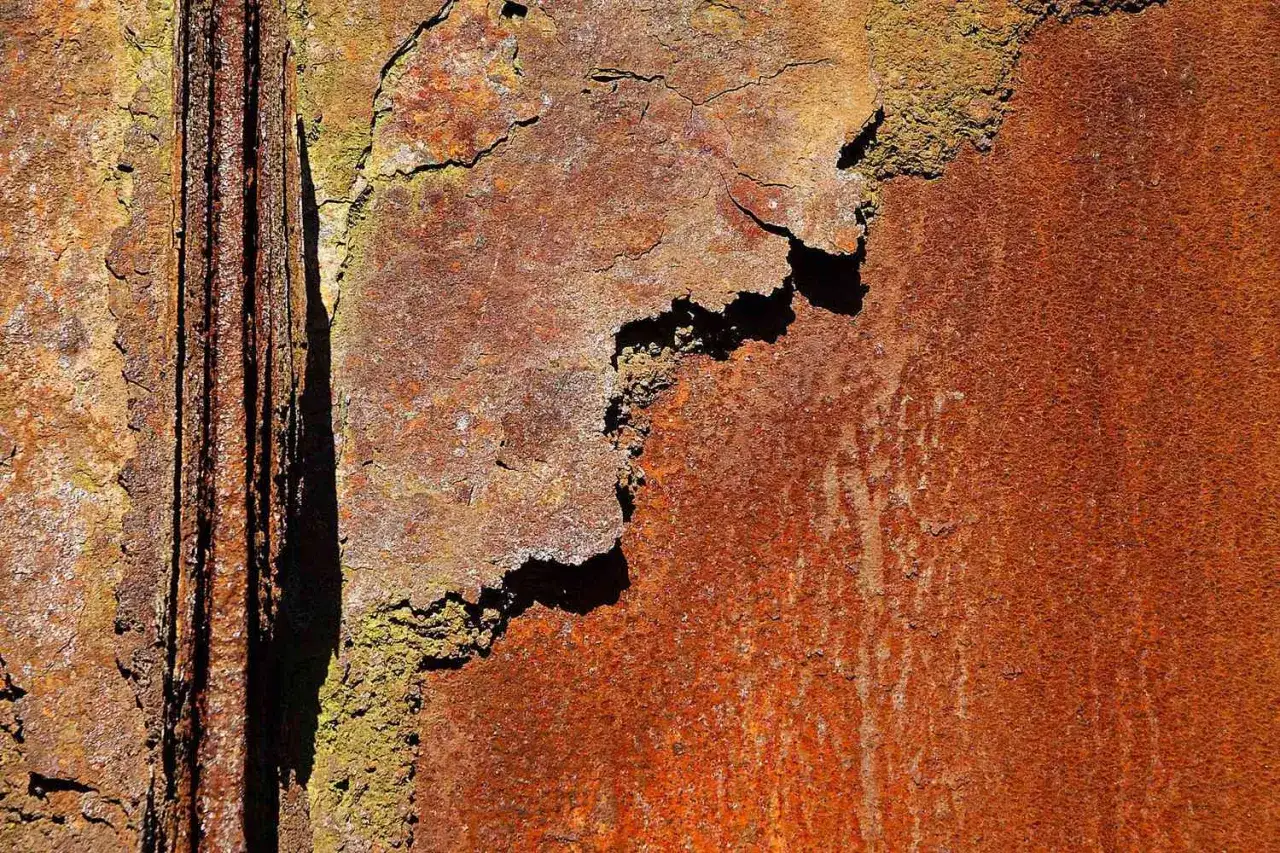 Detailaufnahme von starker chemischer Korrosion an Metall. Rostige Oberflächen mit abgeplatzten Schichten und grünen Ablagerungen.