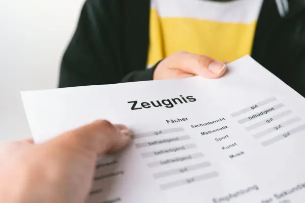 Ein Zeugnis wird überreicht. Die Noten sind gemischt, von "gut" bis "befriedigend", aber keine "ungenügend" Note.