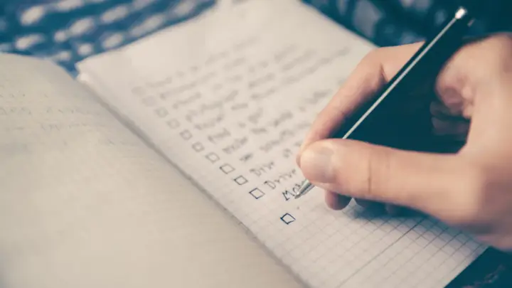 Hand schreibt eine Liste mit Aufgaben auf Englisch. Die Liste enthält Punkte wie "Drive" und "Move", die an eine Aufzählung von Stilmitteln erinnern.