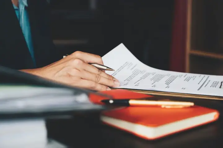 Person überarbeitet ein Resume, um einen Artikel auf Englisch zu schreiben. Ein Stift liegt auf einem Notizbuch.
