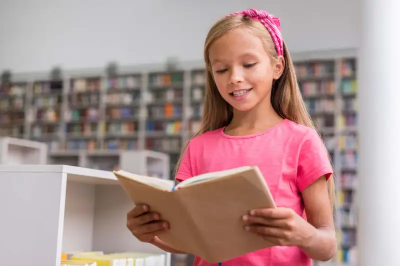 Ein Mädchen mit pinkem Haarband liest in der Schulbibliothek. Ein Beispiel für Leseförderung in der Grundschule, das Freude am Buch zeigt.